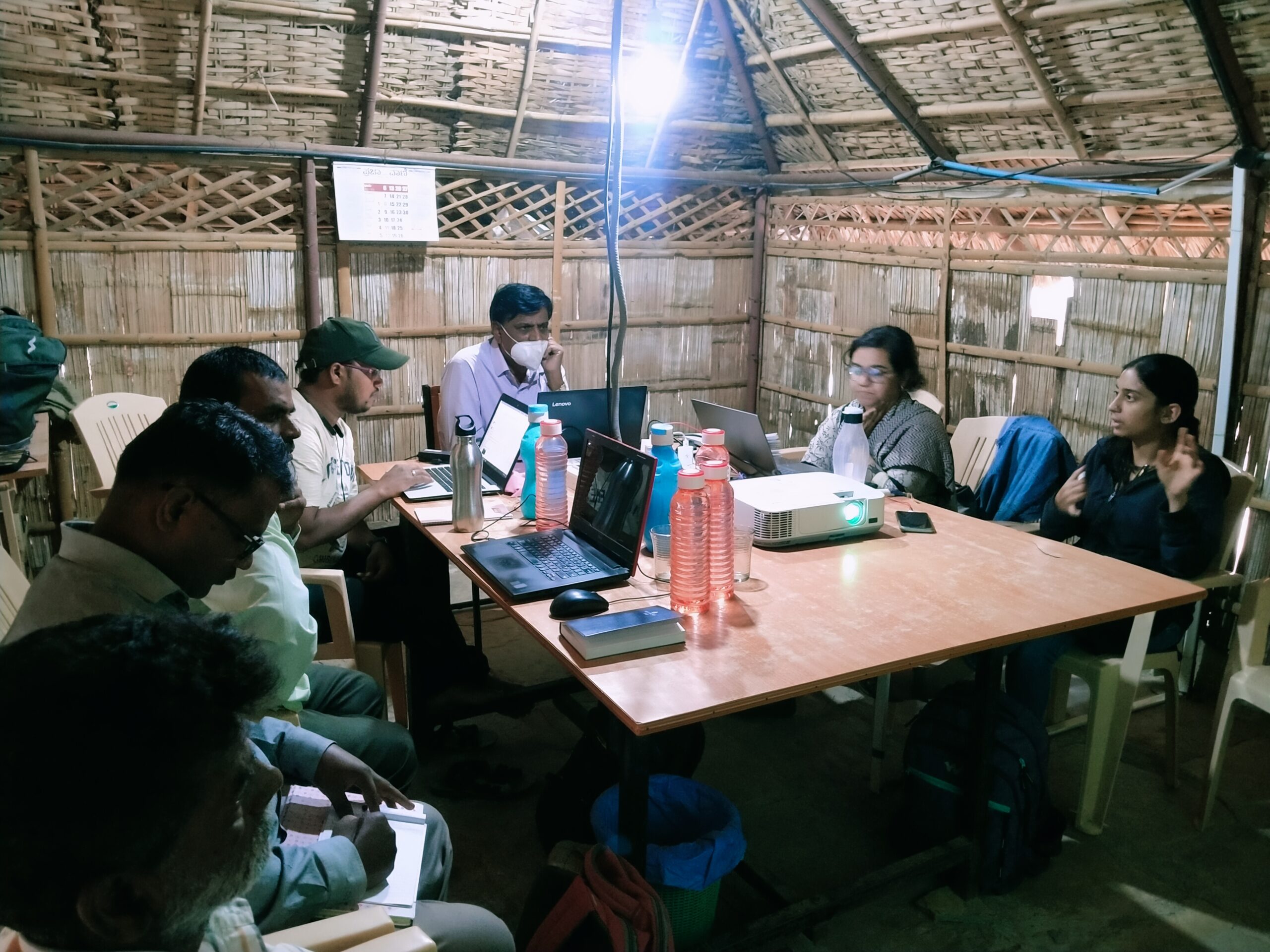 People sitting around a table in a hut, holding a discussion