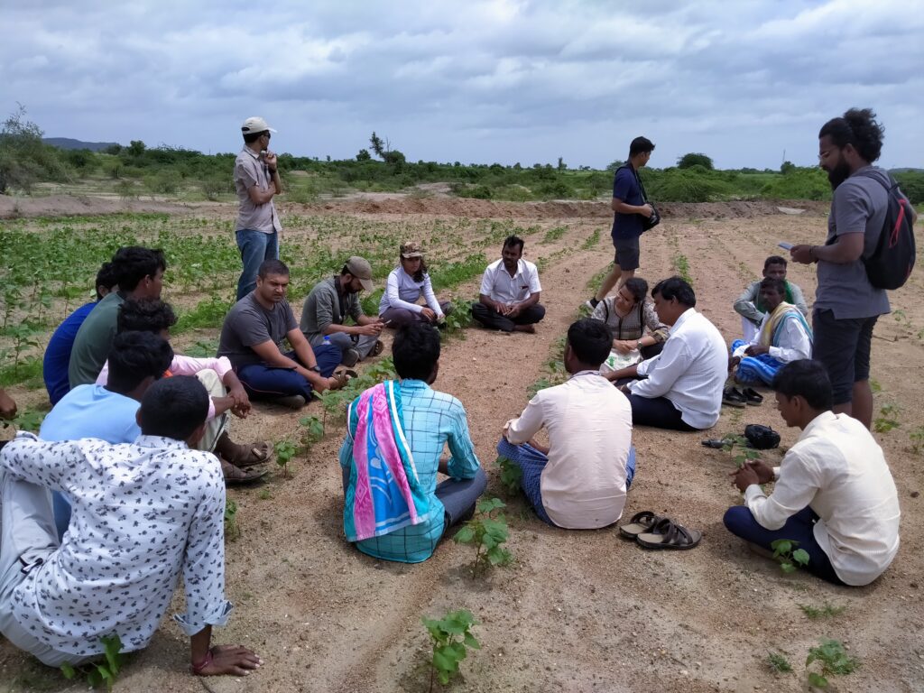 WELL Labs researchers sit with villagers on an open field for a discussion in Raichur
