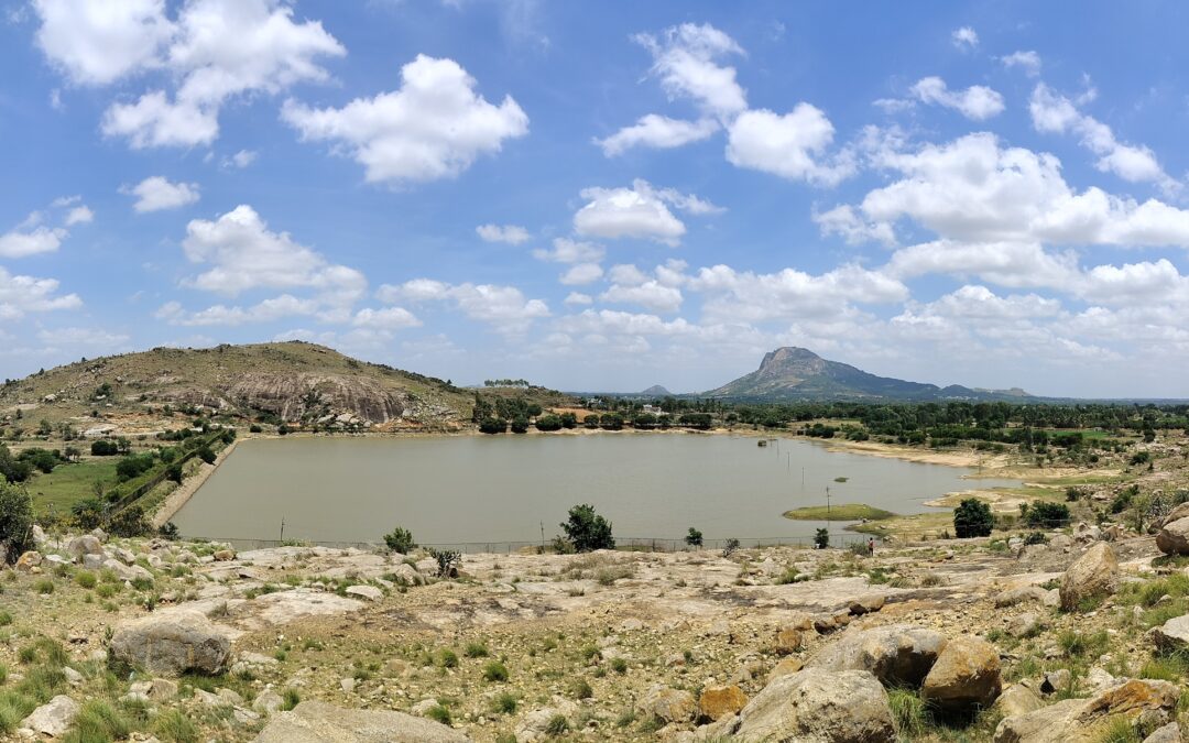 There is a square-shaped lake in the centre of the photo. Above is a blue sky with fluffy clouds and in the foreground is a rocky landscape.