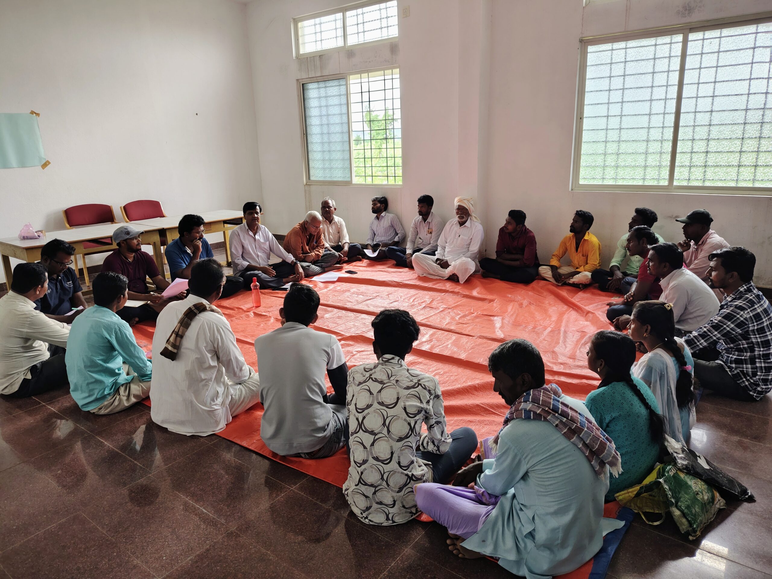 A group of around 20 people sitting in a rectangular shape inside a room