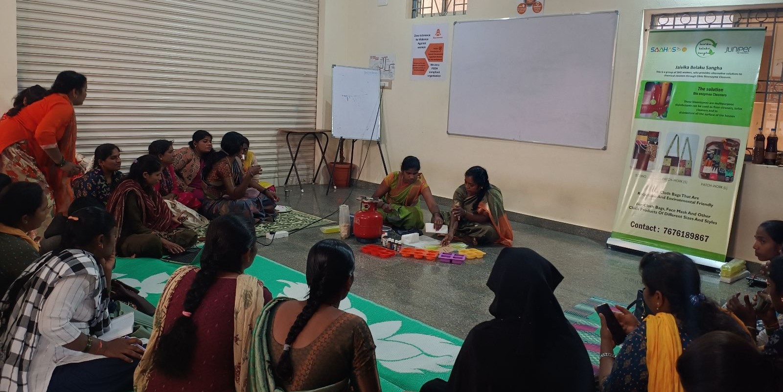 Sahas and Buzz Women collaboration A training session is being conducted in a room. Two women are leading it while 20 women sit around them. Everyone is seated on the floor.