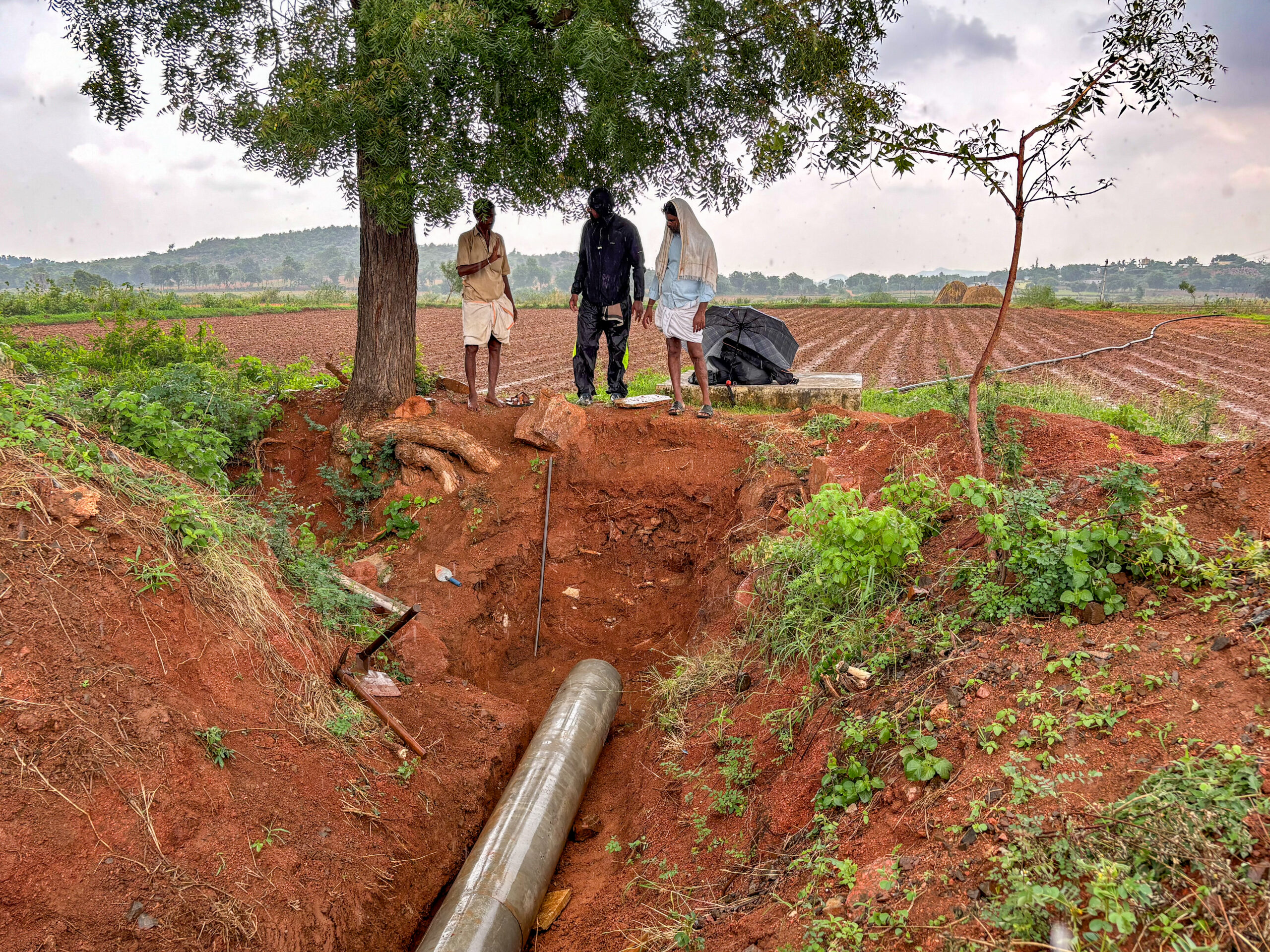 Three people standing above a pipeline in a field