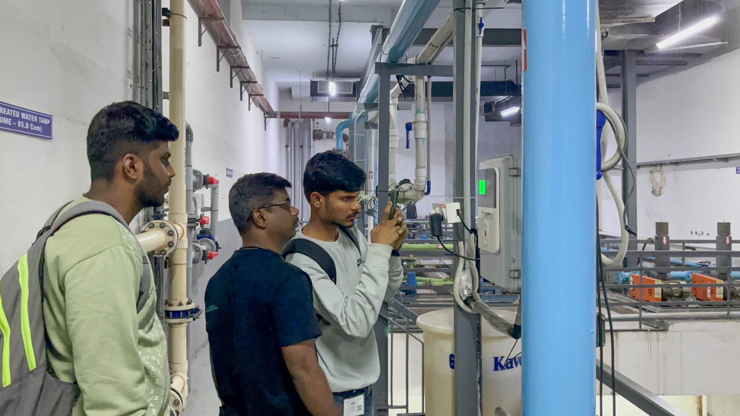 an Image of three men using a phone to click images of a water meter. 